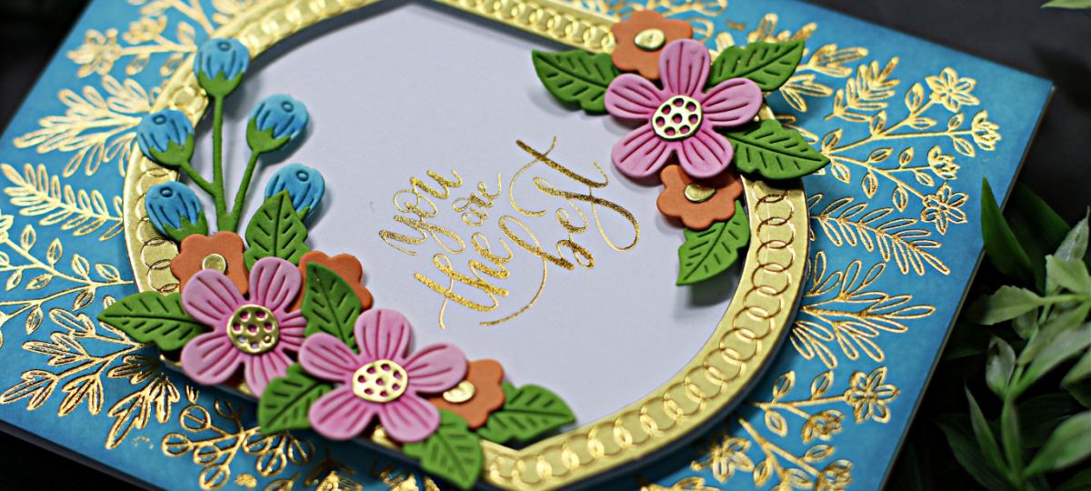 hand made teal card with tiny gold branches inlaid, a gold framed center sentiment surrounded by pink and orange flowers created with new card making supplies from Spellbinders 