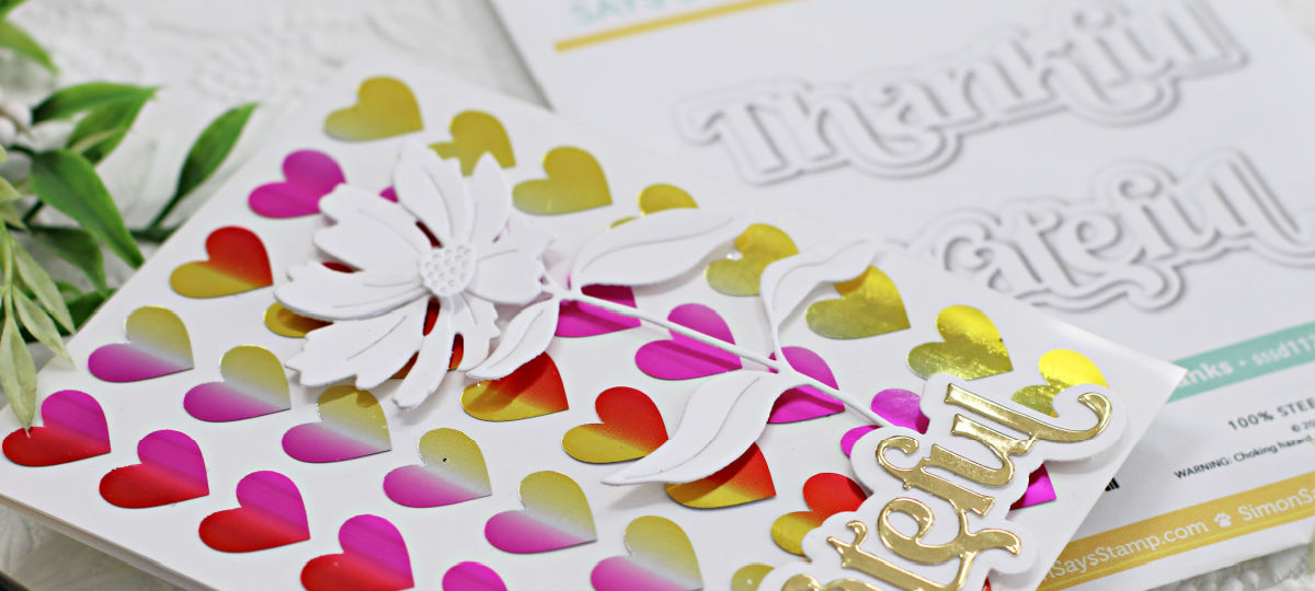 hand made grateful card, with a rainbow foiled heart background, a white die cut flower and a gold and white sentiment created with new card making supplies from Simon Says Stamp