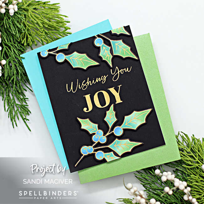 hand made christmas card with a black background, shinny gold sentiment and gold outlined holly with blue berries and three tone green leaves created with new card making products from Spellbinders