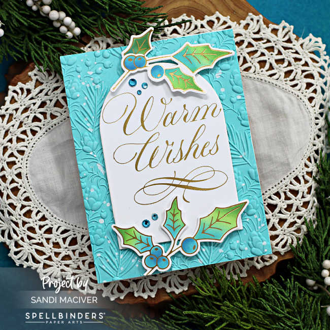 More Christmas in July with ahand made teal christmas card with an embossed background, a large white arch with gold lettering and embellished with die cut holly in blue and green created with the Warm Wishes Copperplate Holiday sentiments from Spellbinders