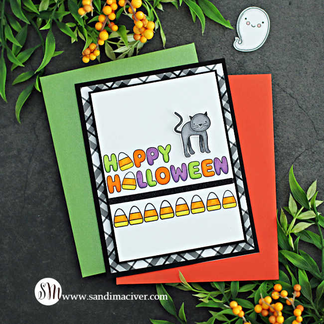 hand made halloween card with happy halloween written across the card, a row of colored candy corn underneath, and a black cat standing on top attached to a black and white plaid card base.