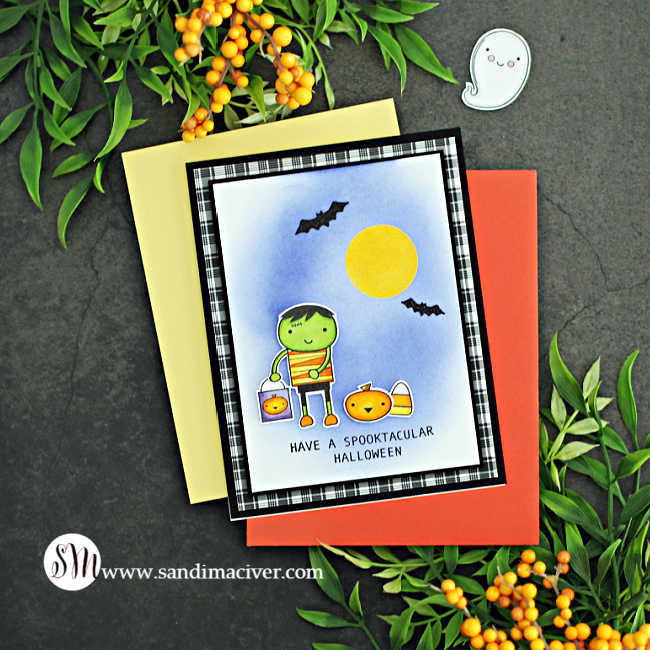 hand made Halloween card with a cartoon Frankenstein holding a goody bag, a little pumpkin and a big candy corn beside him on a purple background with a yellow moon and bats flying overhead.