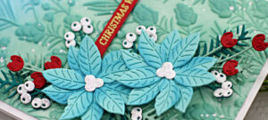 blue and green christmas card with blue poinsettias, red flowers and white berries created with new card making products from Spellbinders