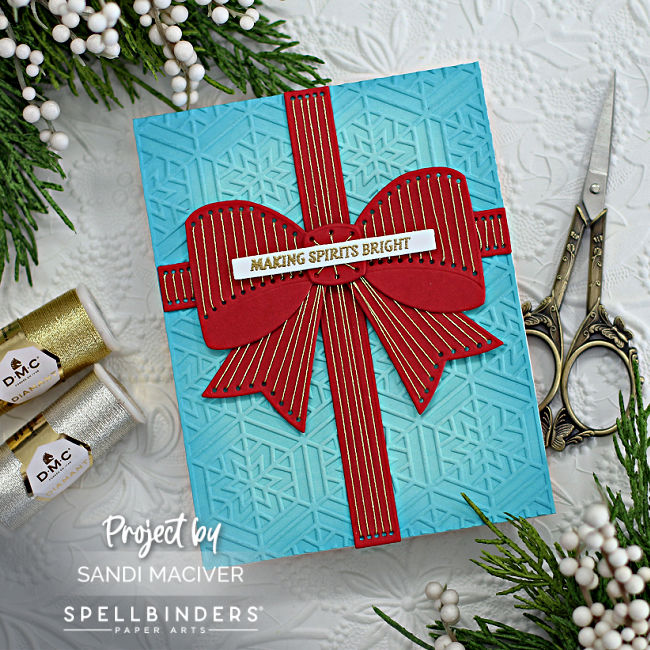 blue and red hand made card with a blue snowflake embossed background and a large red bow stitched with gold thread using new card making products from Spellbinders