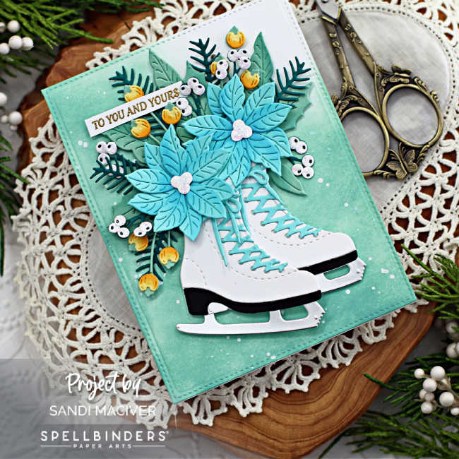 hand made Christmas card with white ice skates and a bouquet of greenery and blue flowers on a pale green splattered background created with new card making products from Spellbinders