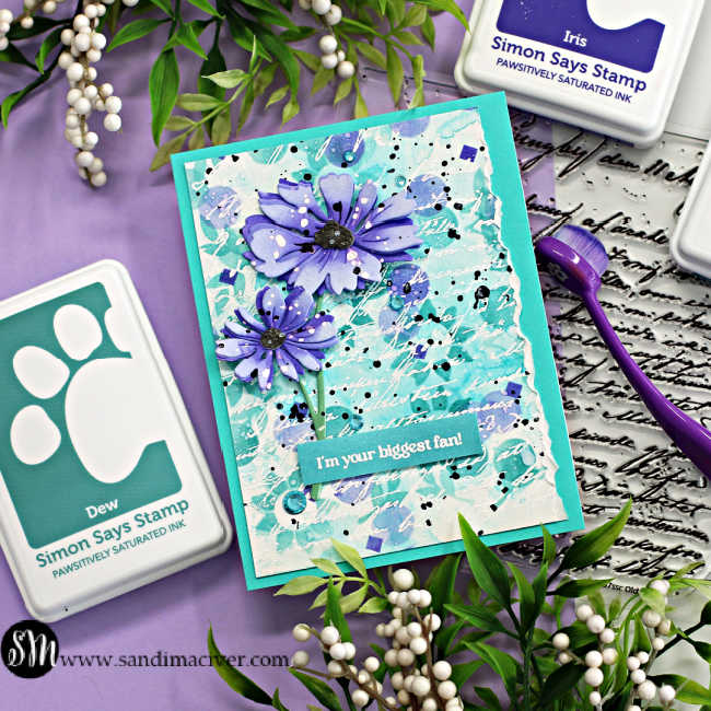 hand made card with a stenciled background in teal and purple with two die cut purple flowers overlaid