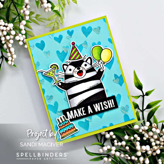 hand made birthday card with a teal background and stenciled hearts, a colored black and white cat holding a drink and balloons and wearing a pink and green party hat