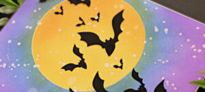 hand made Halloween card with a big yellow moon and a blue and purple sky with a flock of bats flying across it