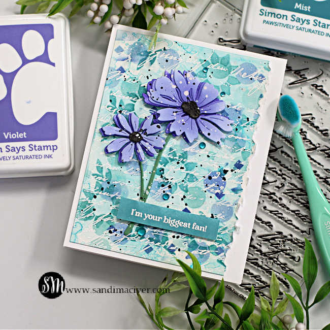 hand made card with a stenciled background in teal and purple with two die cut purple flowers overlaid