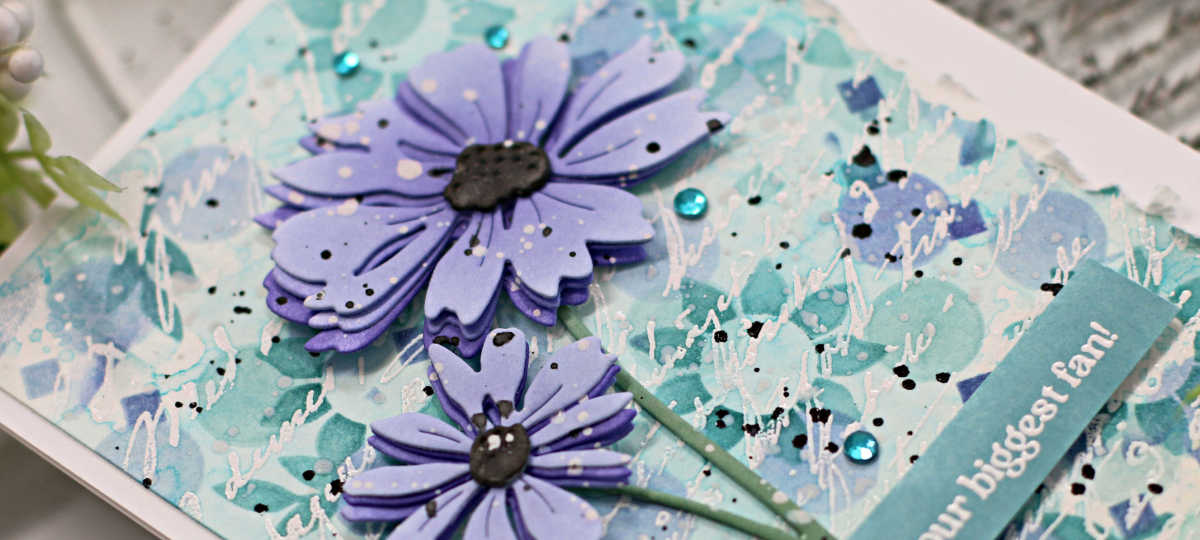 hand made card with a stenciled background in teal and purple with two die cut purple flowers overlaid