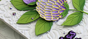 hand made greeting card with a white floral embossed background and large purple flowers with bright green leaves