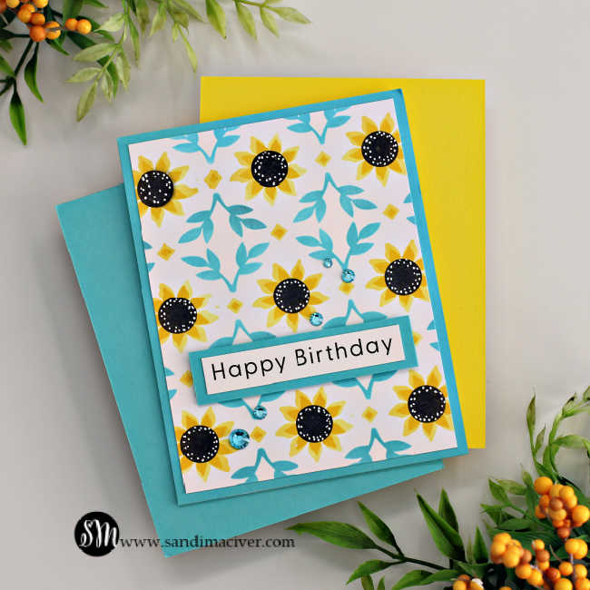 Hand made birthday card with stenciled sunflowers and leaves on a turquoise card base and a turquoise and white sentiment in the center