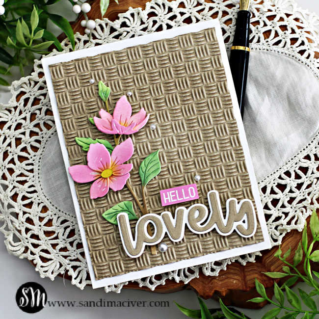 hand made card with a embossed basket weave background with pink and green die cut flowers on the left side and a large die cut sentiment across the bottom