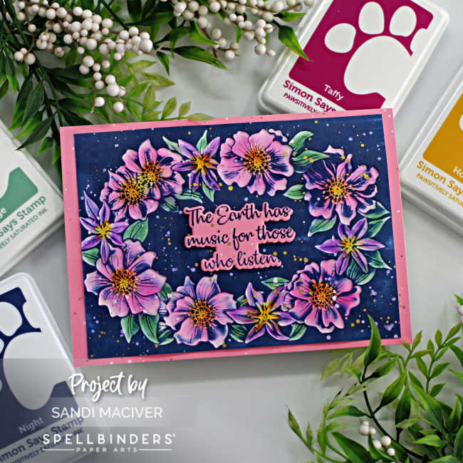 hand made floral card with pink and purple flowers, green leaves and a dark blue background with a pink and blue sentiment in the center