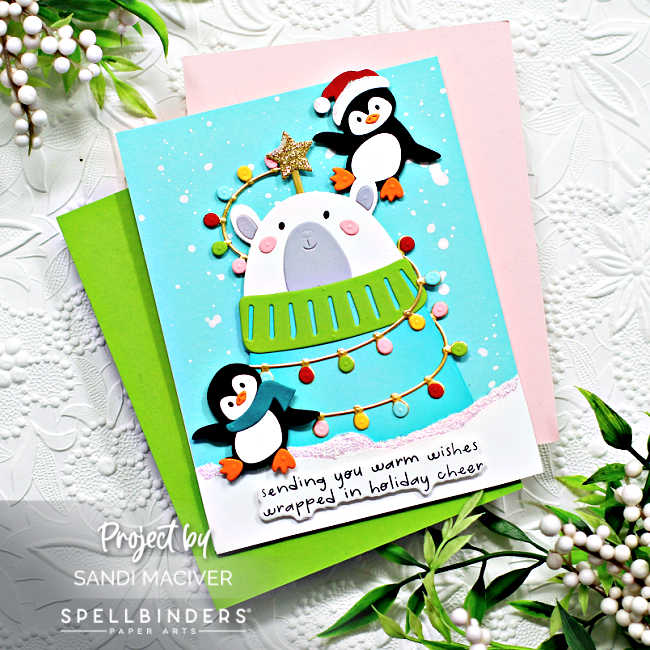 hand made christmas card with a bear in a turquoise sweater being decorated with lights by two penguins