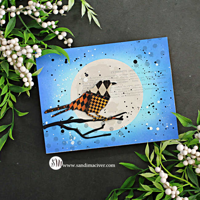 hand made card with a blue sky and a silver moon in the middle. A die cut bird overlay with a quilt pattern of design paper standing on a black branch.