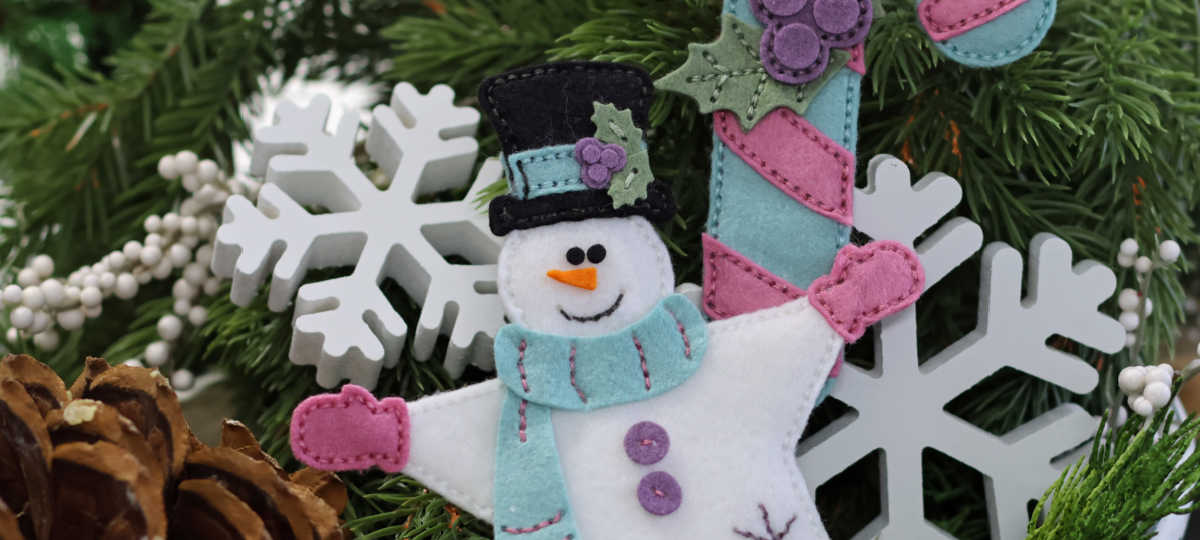 hand stitched star snowman and blue and pink candycane in a dough bowl full of holiday greenery