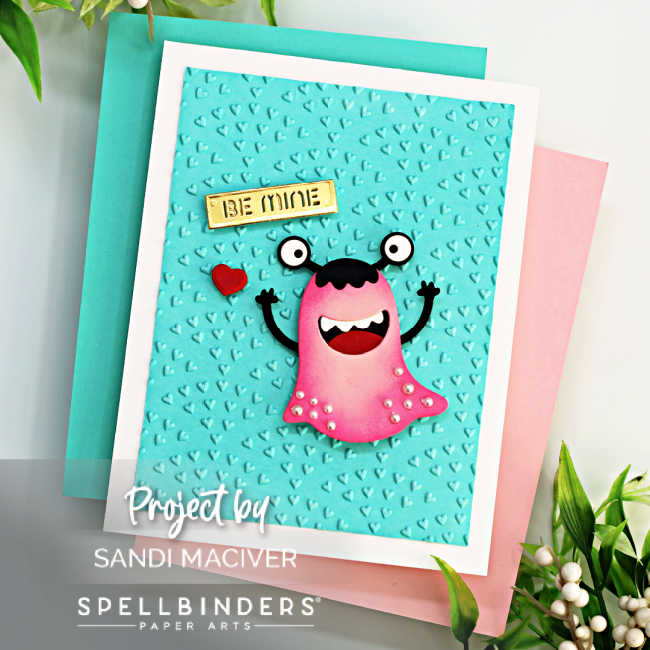 die cut pink and black monster over a teal blue heart embossed background with a gold sentiment