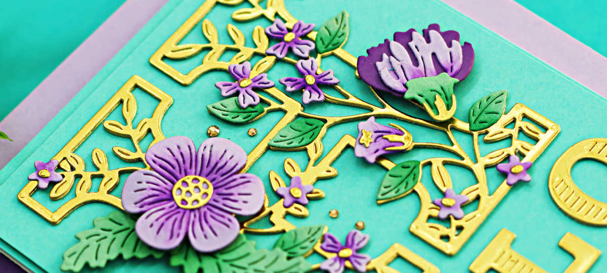 teal colored card with a gold die cut H decorated with purple flowers and green leaves