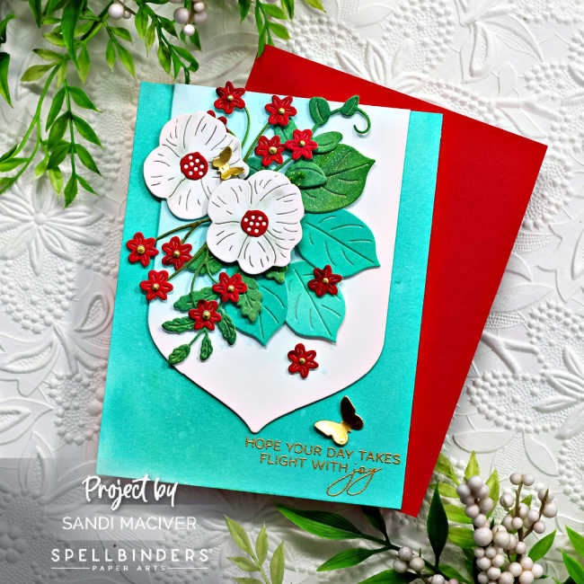 hand made floral card with white and red flowers on a bed of greenery with a turquoise blue background