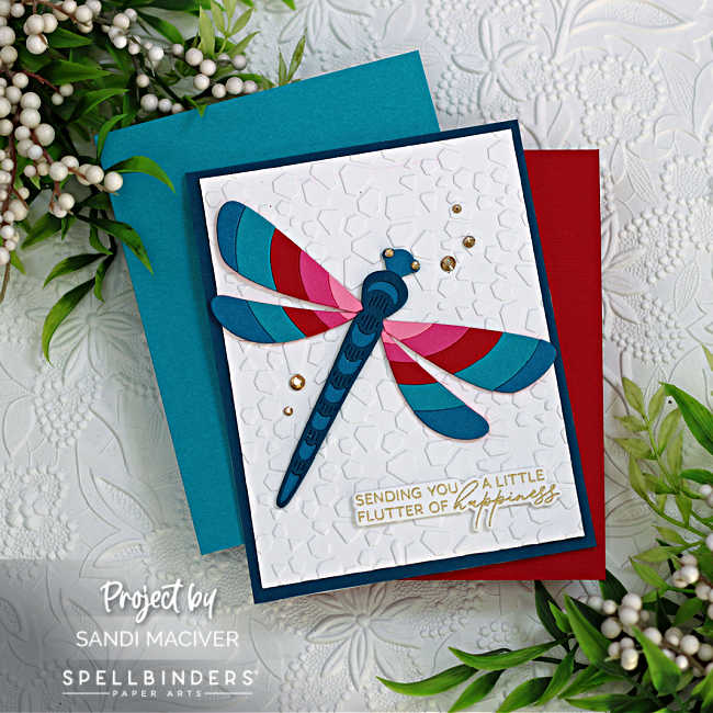 hand made greeting card with a large dragonfly with multi colored wings on top of a white embossed background with a dark blue card base