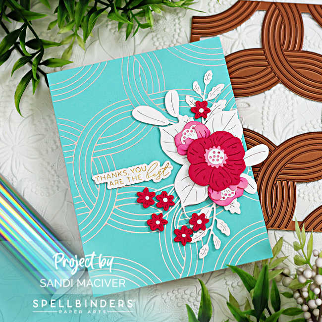 Turquoise hand made card with a silver weave design foiled on the background, with an overlay of pink florals with white die cut leaves and a gold and white sentiment