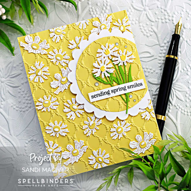 yellow and white embossed card with white flowers scattered over the card front with a scalloped circle on the right hand side with three die cut white daisies with green leaves and stem