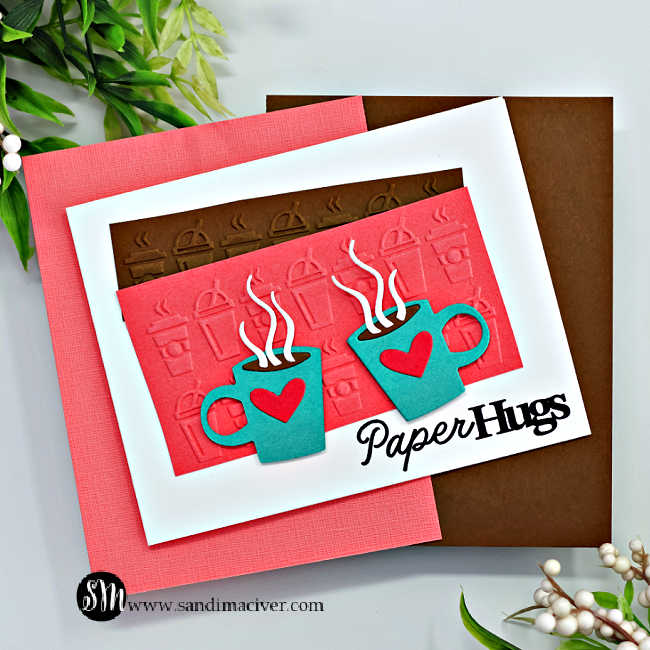 hand made greeting card with embossed coffee mugs in the background in pink and brown, two teal steaming coffee mugs with hearts on the front