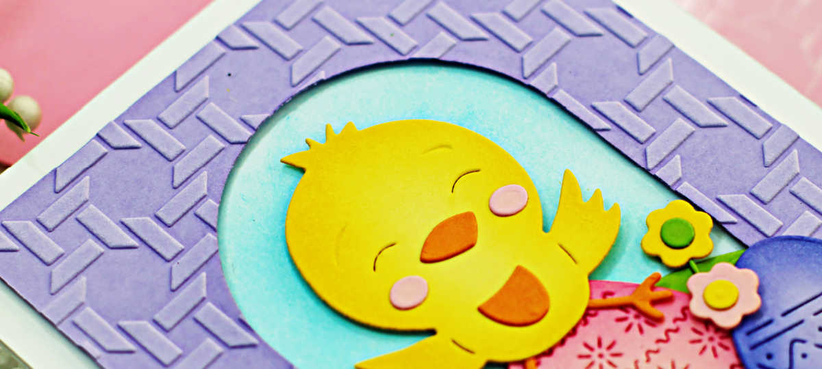 hand made easter card with a purple basket embossed front, and a die cut yellow chick sitting on top of rainbow easter eggs