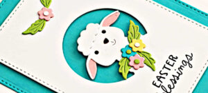 hand made card in teal and white with a cute die cut white lamb surrounded by spring flowers.