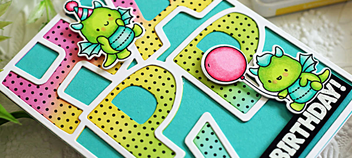 Handmade birthday card featuring Simon Says Stamp Happy Birthday Dragons stamp set. The card showcases two adorable green dragons—one with a pink party hat and the other holding a pink balloon—layered over large, colorful block letters with a rainbow ombré and polka dot pattern. A bold “BIRTHDAY!” sentiment is placed on a black banner at the bottom right corner. Perfect for fun and whimsical birthday card inspiration.