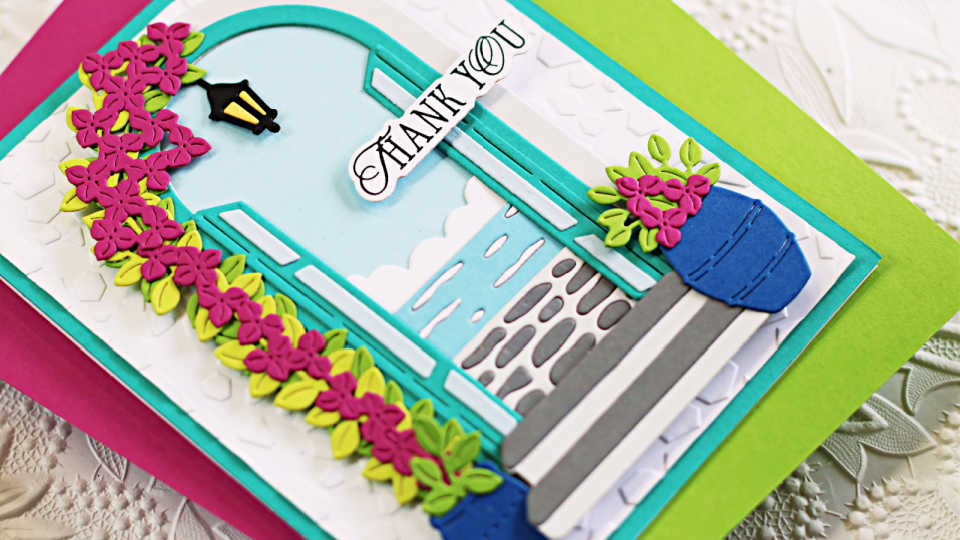 Handmade thank you card using the Spellbinders Beyond the Door die set from the La Dolce Vita release. The design features an arched aqua door opening to a scenic ocean view with clouds, stone steps, and detailed die-cut elements including vibrant pink flowers, lush cascading vines, and blue flower pots. A "Thank You" sentiment adds a personal touch, perfect for card makers who love dimensional die-cutting and scene building.