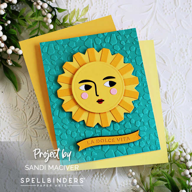 handmade card featuring a stylized yellow sun face with geometric rays, created using Spellbinders La Dolce Vita collection. The sun is layered over a textured turquoise background with an embossed mosaic pattern.