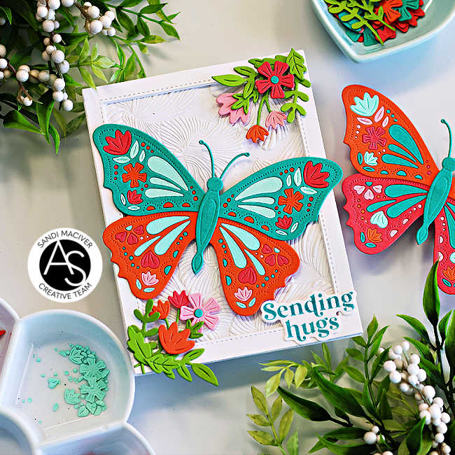 Handmade greeting card featuring a colorful die-cut butterfly design in teal, orange, pink, and aqua, accented with floral die cuts and embossed background texture. Sentiment reads “Sending hugs.” Perfect for spring or summer cardmaking inspiration using Alex Syberia Designs Butterfly Bliss collection.