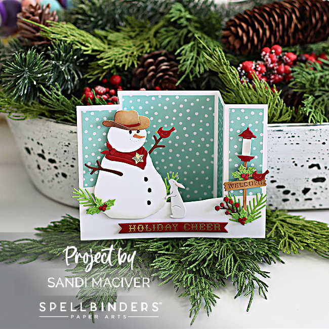 Handmade Christmas bridge card featuring a cowboy snowman with a tan hat, red bandana, and sheriff star, holding a red horseshoe. A white bunny, welcome sign, and snowy landscape add charm, all set against a teal polka dot background. Designed by Sandi MacIver using Spellbinders Country Christmas dies.