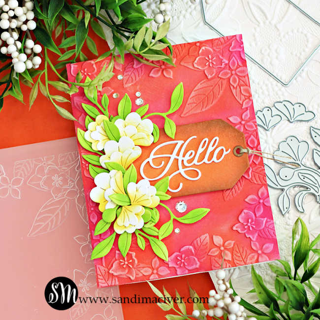 Handmade floral card created with Simon Says Stamp Happy Camper release products. Features an embossed pink and coral background with leafy floral designs, layered white and yellow die-cut flowers with bright green leaves, and a brown ink-blended tag with a white die-cut “Hello” sentiment. Embellished with sparkling clear gems for added dimension and shine.