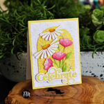 Handmade floral greeting card featuring die-cut white daisies and pink tulips on an embossed yellow arch, layered over a textured white background. Finished with a bold yellow &lsquo;Celebrate&rsquo; sentiment and sparkling gem embellishments. Perfect for spring or summer cardmaking inspiration