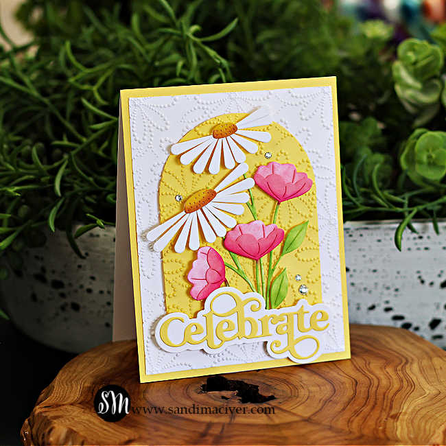 Handmade floral greeting card featuring die-cut white daisies and pink tulips on an embossed yellow arch, layered over a textured white background. Finished with a bold yellow ‘Celebrate’ sentiment and sparkling gem embellishments. Perfect for spring or summer cardmaking inspiration