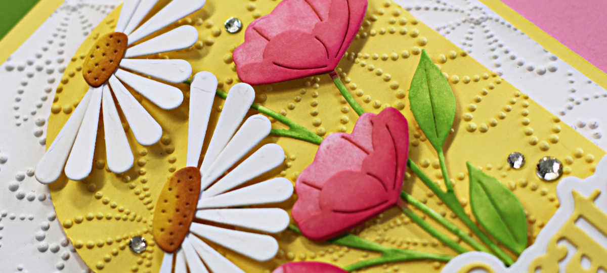 Handmade floral greeting card featuring die-cut white daisies and pink tulips on an embossed yellow arch, layered over a textured white background. Finished with a bold yellow ‘Celebrate’ sentiment and sparkling gem embellishments. Perfect for spring or summer cardmaking inspiration