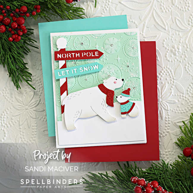Handmade Christmas card featuring a polar bear and cub created with the Spellbinders North Pole Friends die set by Simon Hurley. The bears are dressed in cozy winter accessories—scarves and a hat—in red and aqua. They stand beside a red-and-white striped North Pole signpost with dimensional banners that read "NORTH POLE" and "LET IT SNOW." The background is a soft mint green cardstock embossed with the Starry Snowflakes 3D embossing folder, adding frosty texture. The card is layered over aqua and red mats and styled with festive greenery and berries for a holiday touch.