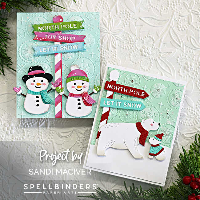 Two handmade Christmas cards created with Spellbinders North Pole Friends die set by Simon Hurley. The left card features two cheerful snowmen in pastel winter hats and scarves standing beside a candy cane-striped North Pole signpost with dimensional banners that read "NORTH POLE," "TOY SHOP," and "LET IT SNOW." The right card showcases a polar bear and cub in red and aqua scarves beneath a red-and-white North Pole sign with similar banners. Both cards have a soft teal embossed background using the Starry Snowflakes Embossing Folder from the July 2025 club kit. Holiday greenery and a white textured backdrop complete the festive scene.