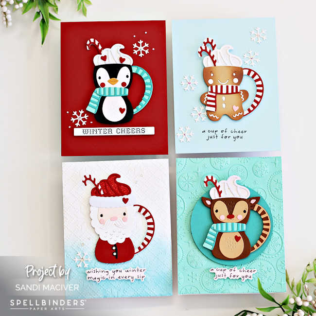 Handmade Christmas cards featuring adorable die-cut mugs shaped like a penguin, gingerbread man, Santa, and reindeer. Each card is embellished with scarves, candy canes, whipped cream, snowflakes, and cheerful holiday sentiments on festive red and blue backgrounds.