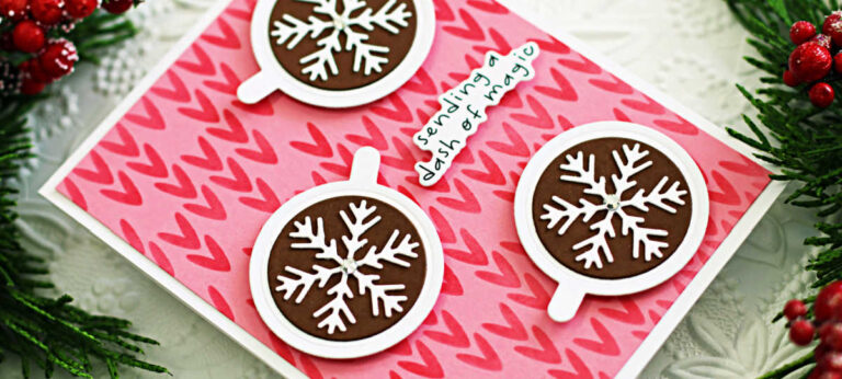 Handmade holiday card featuring a pink stenciled background with bold red heart patterns, three die-cut hot cocoa mugs topped with white snowflake embellishments, and a sentiment reading 'sending a dash of magic,' accented by festive greenery and berries