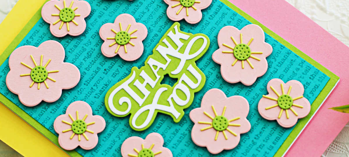 Handmade thank you card created with Simon Says Stamp Groovy Flowers and Showboat Thank You dies. The card features layered pink die-cut flowers with green centers and yellow accents, arranged on a teal panel stamped with the Thank You Text Background stamp. The bold white and green “Thank You” sentiment is centered among the flowers, all layered over a lime green card base for a bright, cheerful design.