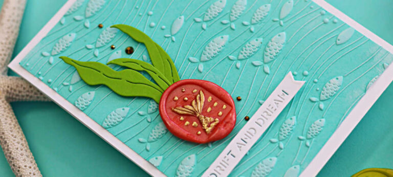 Handmade card featuring the Spellbinders August Embossing Folder Club’s Underwater Waltz design on aqua cardstock, showcasing embossed fish and flowing waves. Embellished with die-cut seaweed in Rainforest cardstock and a coral-colored wax seal from the Wax Seal Club with the Mermaid Tails design, accented in gold. Finished with a white sentiment strip reading “Drift and Dream,” layered on a white A2 card base.