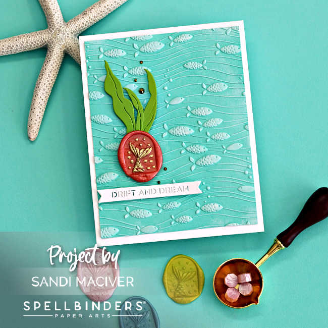 Handmade card featuring the Spellbinders August 2025 Underwater Waltz 3D embossing folder, with embossed fish and wavy lines on aqua cardstock. Embellished with layered seaweed die-cuts in Rainforest green and a coral-colored wax seal from the Wax Seal Club, showcasing the Mermaid Tails design in gold. Finished with a white sentiment strip that reads “Drift and Dream,” and mounted on a white A2 card base. Displayed on a teal background with wax seal tools and a starfish prop.