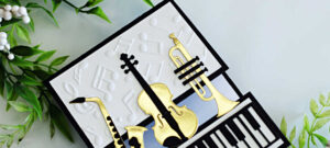 Handmade music-themed card created with Spellbinders Bibi’s Musical Notes Collection. The design features die-cut instruments including a saxophone, violin, and trumpet in gold and black, layered over an embossed musical note background. A bold black and white piano keyboard border completes this elegant musical greeting card.