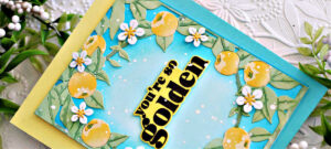 Handmade card created with the Hero Arts You're Golden stamp, die and stencil combo. The card features a turquoise ink-blended background with whit epaint splatters, surrounded by stenciled green leaves, golden yellow applies and white blossoms. The bold sentiment "you're so golden" is stamped in black on an ink-blended yellow layer, creating a fresh, vibrant, summer-inspired design.