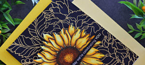 Handmade card featuring the Simon Says Stamp Sunflower Dreams background stamp. The large sunflower in the center is colored with Copic markers in vibrant yellows and browns. The background design is gold heat-embossed onto black cardstock, creating an elegant contrast. A slim sentiment strip reads “today we’re celebrating YOU,” completing the bold and celebratory design.