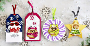 Four handmade holiday gift tags created with the Spellbinders Merry Mischief release. Designs include Santa’s suit over a chimney with snowflakes and sentiment, a cute critter bundled in a scarf and hat on an embossed snowflake background, a round tag with a striped backdrop featuring another winter critter, and a star-shaped tag with a festive animal dressed as a Christmas tree. Each tag is finished with colorful ribbons and surrounded by die-cut snowflakes for a festive holiday display.